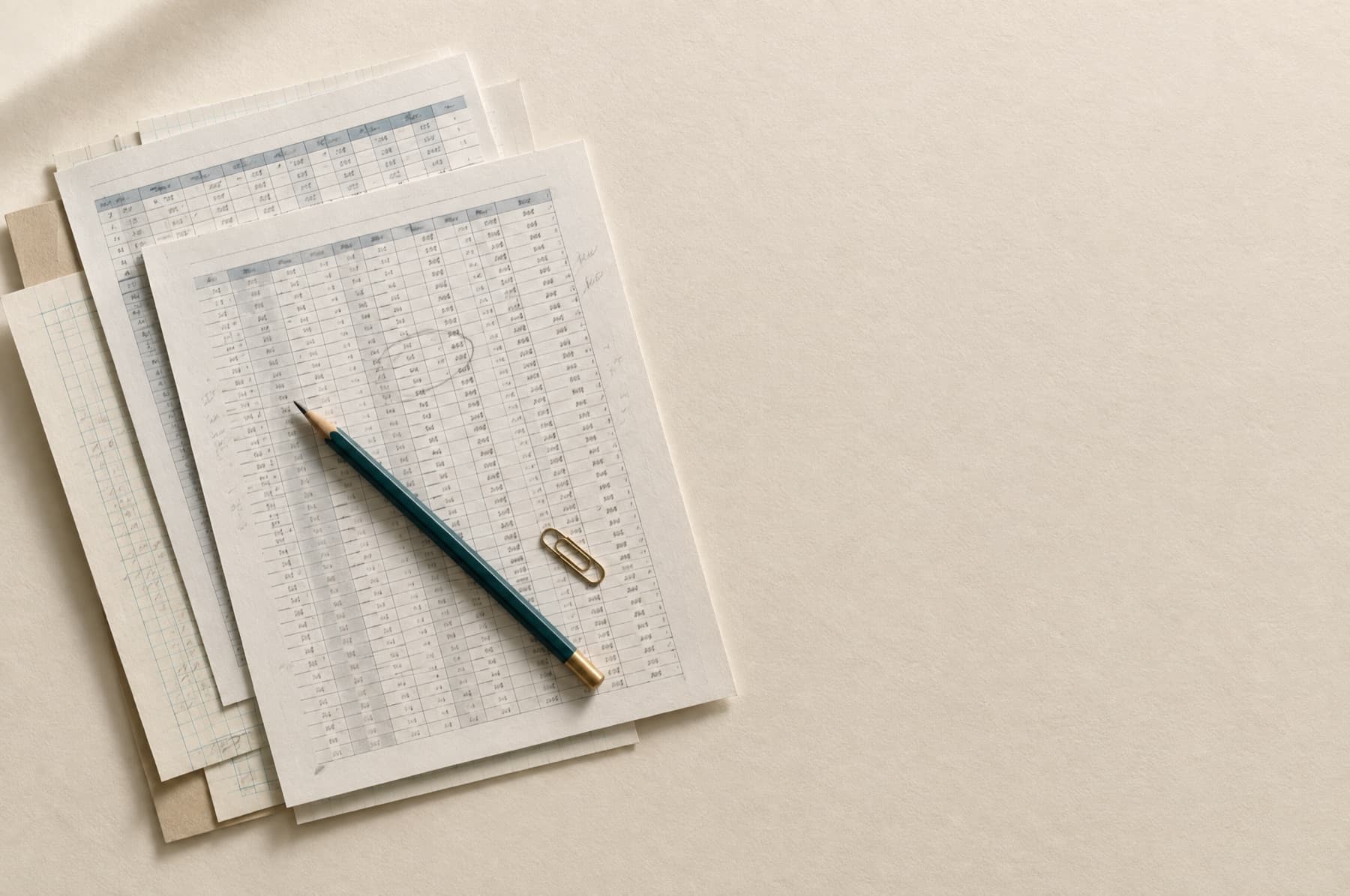 A stack of printed spreadsheets with pencil annotations and a teal pencil.